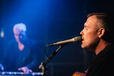 Sebastian Hegener singt bei einem Auftritt in ein Mikrofon und spielt Gitarre.