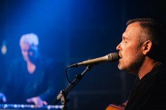 Sebastian Hegener singt bei einem Auftritt in ein Mikrofon und spielt Gitarre.