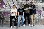 Vier Mitglieder der Band Seltaebs vor einer mit Graffiti besprühten Backsteinwand.