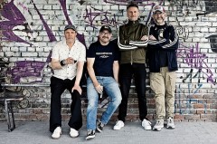 Vier Mitglieder der Band Seltaebs vor einer mit Graffiti besprühten Backsteinwand.