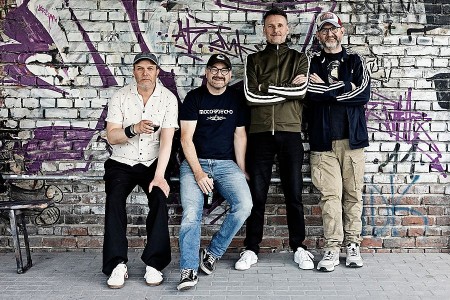 Vier Mitglieder der Band Seltaebs vor einer mit Graffiti besprühten Backsteinwand.