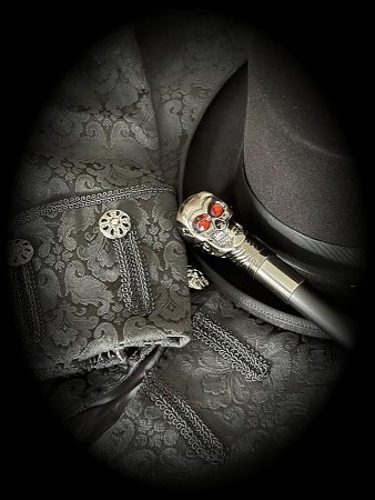 Schwarzer Zylinder, gemusterte schwarze Kleidung und ein Gehstock mit Totenkopfgriff.
