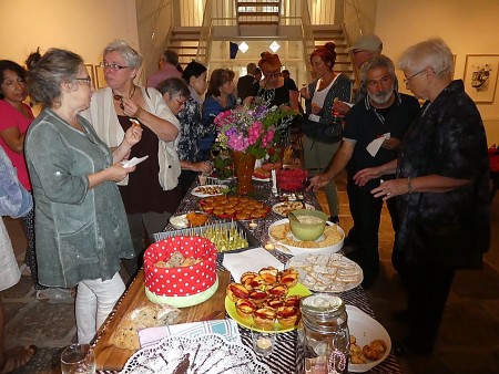 Gäste stehen in einem Ausstellungsraum an einem langen Buffet mit süßen und herzhaften Speisen.