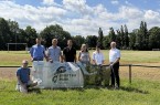 Sieben Personen posieren an einem Sportplatz mit einem Schild „Sport im Park Vlotho“.