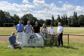 Sieben Personen posieren an einem Sportplatz mit einem Schild „Sport im Park Vlotho“.