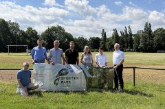 Sieben Personen posieren an einem Sportplatz mit einem Schild „Sport im Park Vlotho“.
