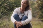 Frau sitzt auf einem Baumstamm in einer ruhigen, naturnahen Umgebung.