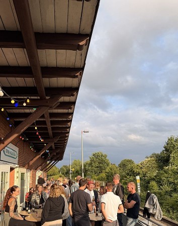 Gäste auf der Terrasse des Weberei-Bahnhofs bei einem sommerlichen Abend mit Getränken und Musik