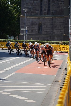 Eine Gruppe von Radrennfahrerinnen fährt bei einem Kriteriumsrennen in einer Innenstadt durch eine Kurve.