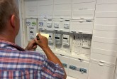 Mann notiert Zählerdaten vor einem geöffneten Stromzähler- und Verteilerkasten