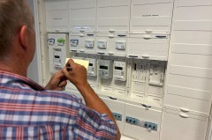 Mann notiert Zählerdaten vor einem geöffneten Stromzähler- und Verteilerkasten
