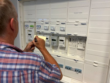 Mann notiert Zählerdaten vor einem geöffneten Stromzähler- und Verteilerkasten