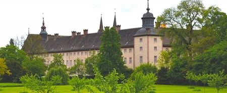Historische Kloster- und Schlossanlage Corvey hinter einer grünen Parkanlage mit Bäumen.
