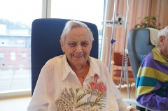 Ältere Patientin sitzt lächelnd im Wohnzimmer-Projekt im Klinikum Gütersloh.