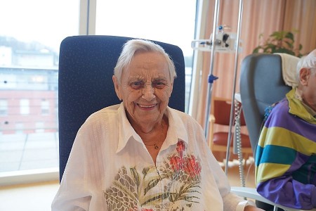 Ältere Patientin sitzt lächelnd im Wohnzimmer-Projekt im Klinikum Gütersloh.