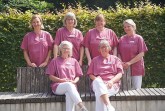Sechs Mitarbeiterinnen des Wohnzimmer-Projekts im Klinikum Gütersloh in rosa Pflegekleidung vor einer Hecke.