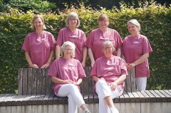 Sechs Mitarbeiterinnen des Wohnzimmer-Projekts im Klinikum Gütersloh in rosa Pflegekleidung vor einer Hecke.
