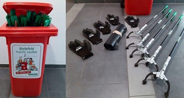 Roter CleanCaddy der Stadt Bielefeld sowie Greifzangen und Handschuhe für Müllsammelaktionen.