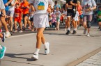 Kinder laufen bei einem Schülerlauf auf einer abgesperrten Strecke; im Vordergrund läuft ein Kind in weißer Sportkleidung.