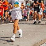 Kinder laufen bei einem Schülerlauf auf einer abgesperrten Strecke; im Vordergrund läuft ein Kind in weißer Sportkleidung.