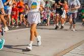 Kinder laufen bei einem Schülerlauf auf einer abgesperrten Strecke; im Vordergrund läuft ein Kind in weißer Sportkleidung.