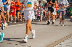 Kinder laufen bei einem Schülerlauf auf einer abgesperrten Strecke; im Vordergrund läuft ein Kind in weißer Sportkleidung.