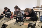 Drei junge Personen arbeiten an Lötstationen in einem Seminarraum.