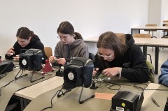 Drei junge Personen arbeiten an Lötstationen in einem Seminarraum.