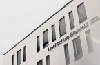 Außenansicht des Gebäudes der Hochschule Bielefeld am Campus Gütersloh mit Fensterreihe und dem Schriftzug „Hochschule Bielefeld – Campus Gütersloh“.