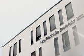 Außenansicht des Gebäudes der Hochschule Bielefeld am Campus Gütersloh mit Fensterreihe und dem Schriftzug „Hochschule Bielefeld – Campus Gütersloh“.