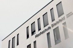 Außenansicht des Gebäudes der Hochschule Bielefeld am Campus Gütersloh mit Fensterreihe und dem Schriftzug „Hochschule Bielefeld – Campus Gütersloh“.