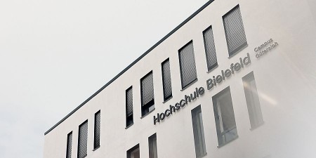 Außenansicht des Gebäudes der Hochschule Bielefeld am Campus Gütersloh mit Fensterreihe und dem Schriftzug „Hochschule Bielefeld – Campus Gütersloh“.