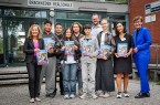 chülerinnen und Schüler der Brackweder Realschule halten gemeinsam mit Erwachsenen Exemplare des IHK-Ausbildungsatlas 2027 vor dem Schulgebäude.