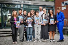 chülerinnen und Schüler der Brackweder Realschule halten gemeinsam mit Erwachsenen Exemplare des IHK-Ausbildungsatlas 2027 vor dem Schulgebäude.