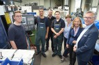Auszubildende und Vertreter der IHK stehen bei HAKU in Halle gemeinsam in einer Produktionshalle vor CNC-Maschinen.