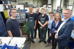 Auszubildende und Vertreter der IHK stehen bei HAKU in Halle gemeinsam in einer Produktionshalle vor CNC-Maschinen.