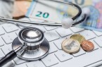 Stethoskop auf einer Computertastatur neben Euro-Banknoten und Münzen