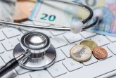 Stethoskop auf einer Computertastatur neben Euro-Banknoten und Münzen