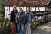 Drei Frauen stehen vor einem historischen Fachwerkgebäude mit Holzsteg und Ziegeldach.