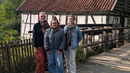 Drei Frauen stehen vor einem historischen Fachwerkgebäude mit Holzsteg und Ziegeldach.