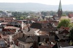 Blick über die Dächer der Mindener Innenstadt mit Kirchturm und bewaldeten Höhen im Hintergrund.