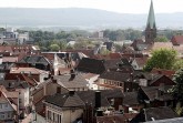 Blick über die Dächer der Mindener Innenstadt mit Kirchturm und bewaldeten Höhen im Hintergrund.