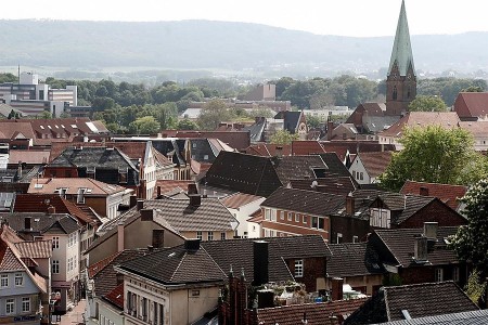 Blick über die Dächer der Mindener Innenstadt mit Kirchturm und bewaldeten Höhen im Hintergrund.