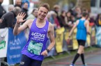 Läufer im violetten Trikot winkt während eines Straßenlaufs am Streckenrand in die Kamera.