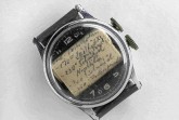 Alte Armbanduhr mit handgeschriebenem Spickzettel unter dem Uhrglas.