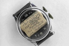Alte Armbanduhr mit handgeschriebenem Spickzettel unter dem Uhrglas.