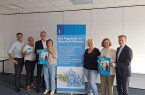 Sieben Beteiligte von DeineDiakonie und der Sparkassenstiftung stehen neben einem Banner mit Angeboten des Netzwerks Demenz und halten Veranstaltungsplakate.