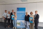 Sieben Beteiligte von DeineDiakonie und der Sparkassenstiftung stehen neben einem Banner mit Angeboten des Netzwerks Demenz und halten Veranstaltungsplakate.