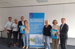 Sieben Beteiligte von DeineDiakonie und der Sparkassenstiftung stehen neben einem Banner mit Angeboten des Netzwerks Demenz und halten Veranstaltungsplakate.